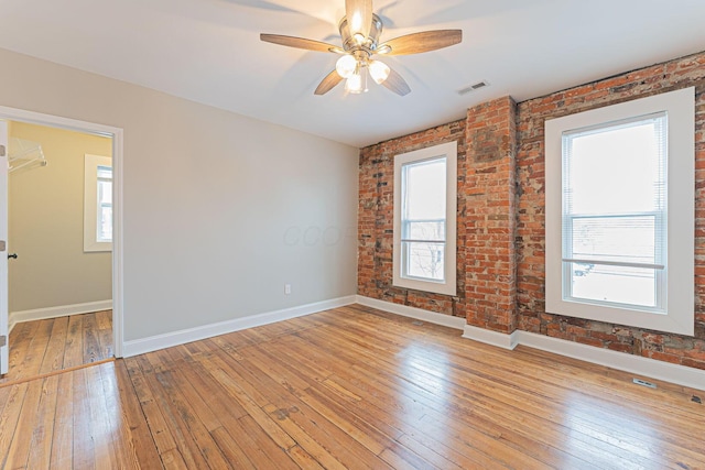 empty room featuring plenty of natural light, brick wall, and light wood-type flooring