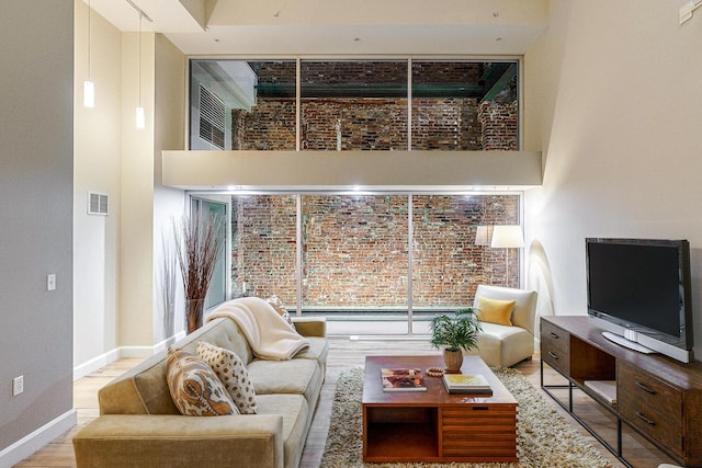 living room with brick wall, light hardwood / wood-style flooring, and a high ceiling