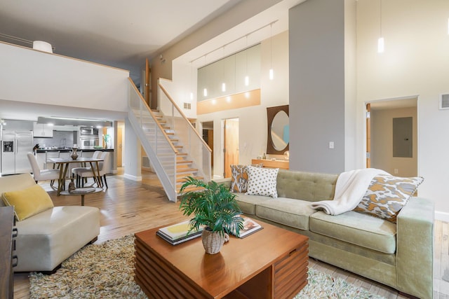 living room with a towering ceiling, sink, electric panel, and light hardwood / wood-style flooring