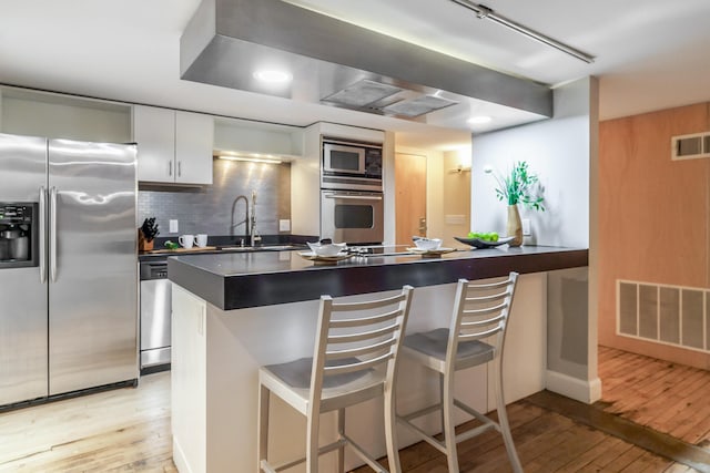 kitchen with sink, white cabinetry, light wood-type flooring, appliances with stainless steel finishes, and a kitchen breakfast bar