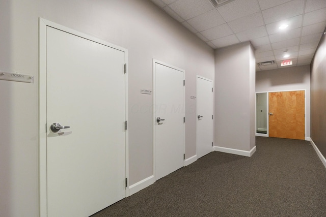 hall featuring a drop ceiling and dark carpet