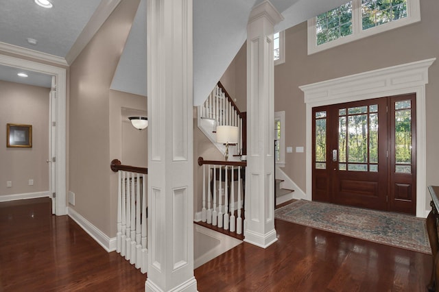 entryway with dark wood-type flooring, crown molding, decorative columns, and a high ceiling