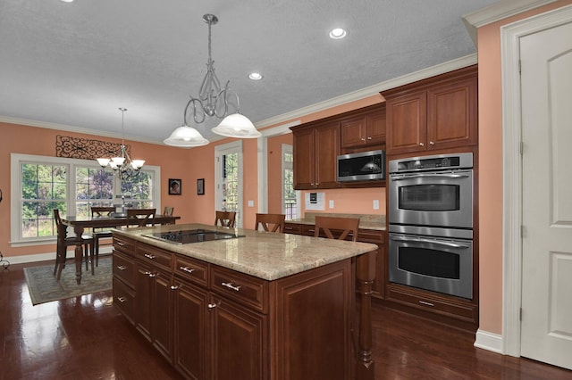 kitchen featuring dark wood-type flooring, light stone counters, decorative light fixtures, a center island with sink, and stainless steel appliances