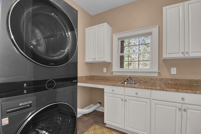 laundry area with cabinets, stacked washer and dryer, tile patterned flooring, and sink