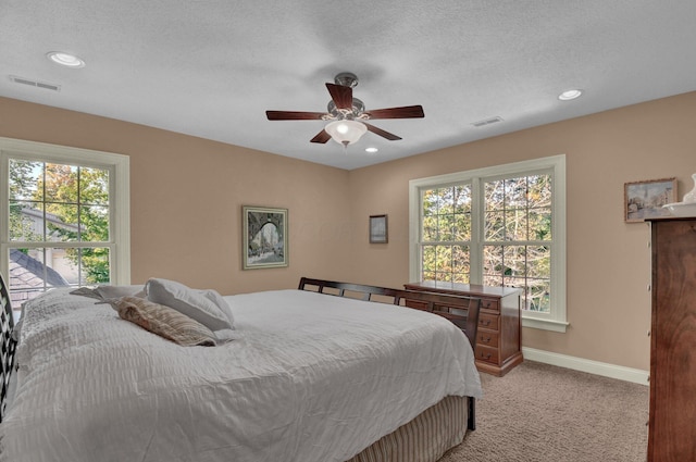 bedroom featuring ceiling fan, light colored carpet, multiple windows, and a textured ceiling