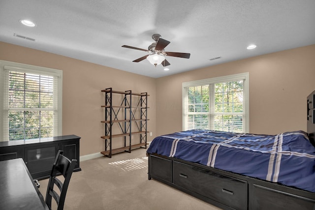 bedroom with ceiling fan, light colored carpet, and a textured ceiling