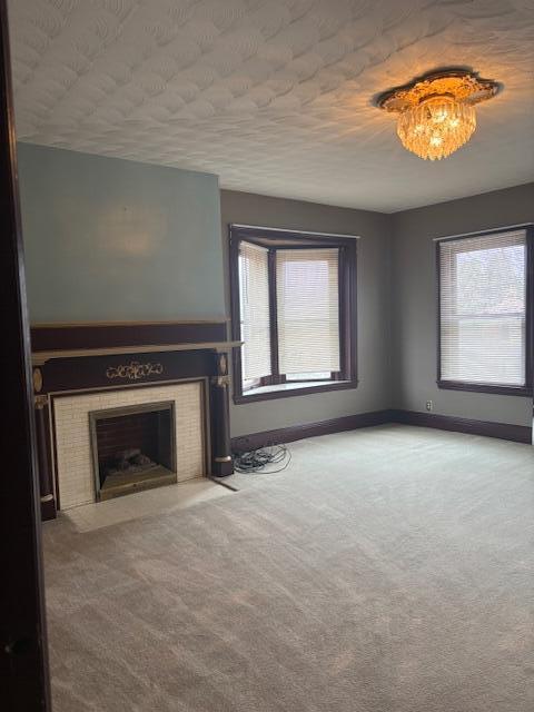 unfurnished living room with a tile fireplace, a chandelier, a textured ceiling, and carpet flooring