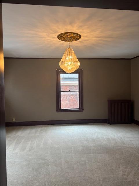 unfurnished room with radiator heating unit, a chandelier, and light carpet