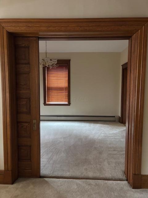 empty room with an inviting chandelier, light colored carpet, and a baseboard heating unit