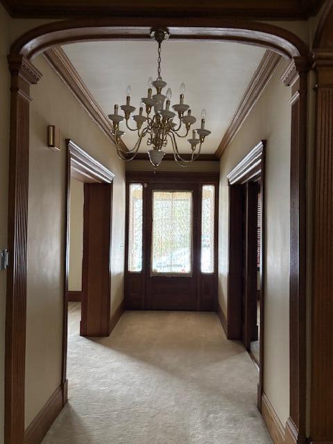 foyer entrance with light carpet, ornamental molding, decorative columns, and an inviting chandelier