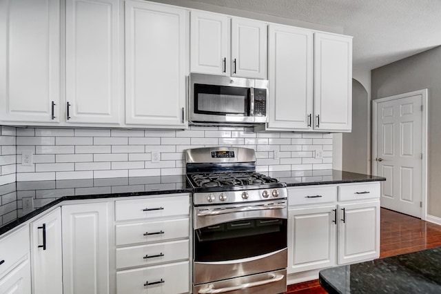 kitchen featuring tasteful backsplash, dark stone countertops, dark hardwood / wood-style flooring, stainless steel appliances, and white cabinets