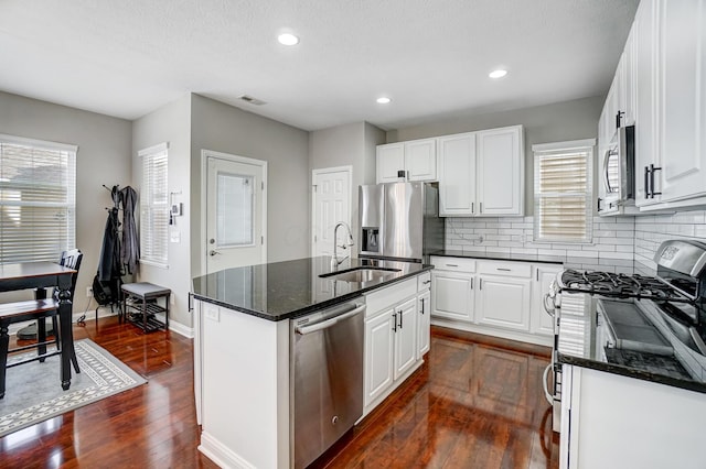 kitchen featuring sink, stainless steel appliances, white cabinets, a center island with sink, and dark stone counters