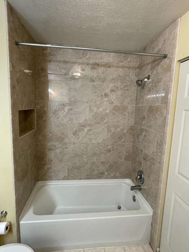 bathroom with tiled shower / bath combo, tile patterned floors, a textured ceiling, and toilet