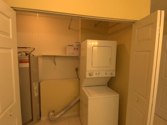 clothes washing area featuring light tile patterned flooring, stacked washer and clothes dryer, and electric water heater