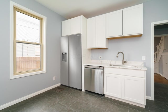 kitchen with white cabinetry, stainless steel dishwasher, sink, and dark tile patterned floors