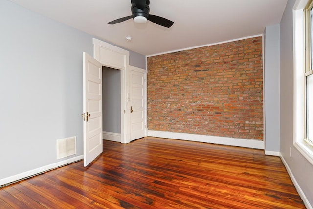 unfurnished bedroom with brick wall, dark hardwood / wood-style floors, and ceiling fan