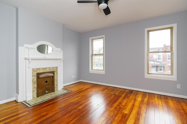 unfurnished living room featuring ceiling fan, wood-type flooring, and a tiled fireplace