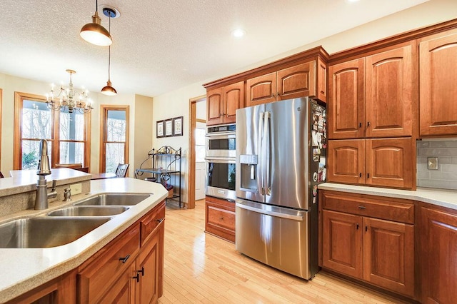 kitchen with sink, tasteful backsplash, hanging light fixtures, appliances with stainless steel finishes, and light hardwood / wood-style floors