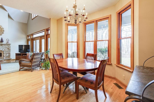 dining room featuring lofted ceiling, a notable chandelier, a fireplace, and light wood-type flooring