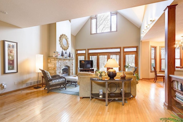 living room featuring a fireplace, high vaulted ceiling, light hardwood / wood-style flooring, and a notable chandelier