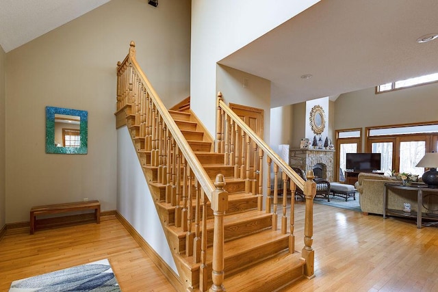 staircase featuring wood-type flooring, a stone fireplace, and high vaulted ceiling