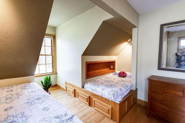 bedroom with lofted ceiling, a textured ceiling, and light wood-type flooring