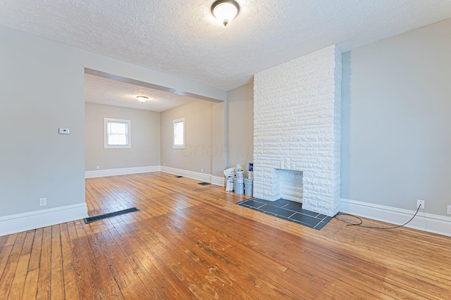 unfurnished living room featuring wood-type flooring, a large fireplace, and a textured ceiling