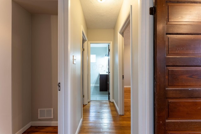 hall with a textured ceiling and light hardwood / wood-style flooring