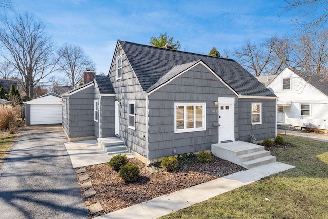 view of front of property featuring a detached garage, an outbuilding, roof with shingles, and a chimney