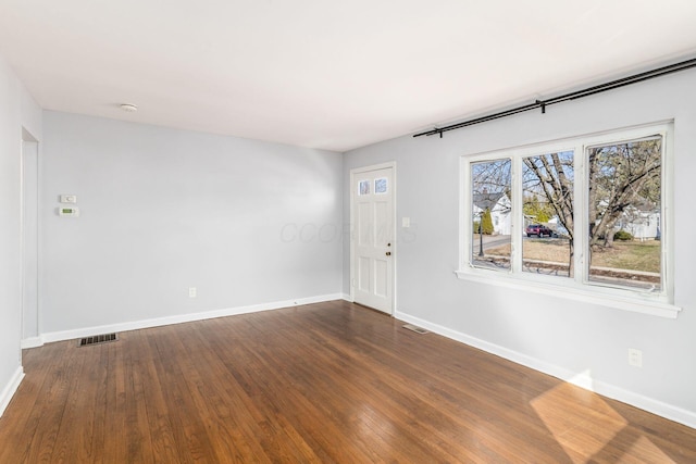 empty room with dark wood finished floors, visible vents, and baseboards