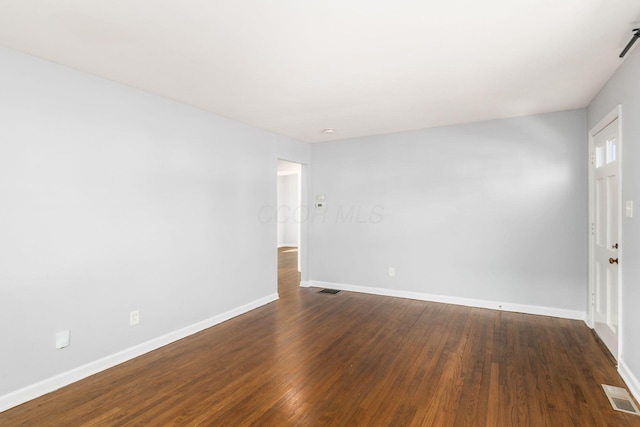 empty room featuring visible vents, baseboards, and dark wood-type flooring