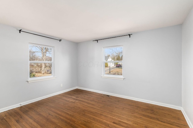 spare room with visible vents, a healthy amount of sunlight, baseboards, and dark wood-style flooring