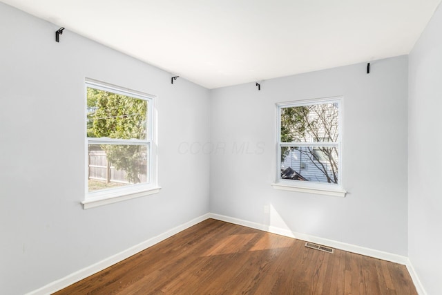 empty room with dark wood finished floors, visible vents, and baseboards