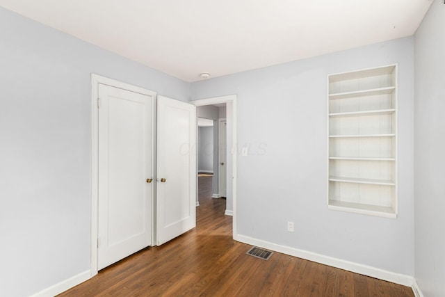 unfurnished bedroom featuring wood finished floors, baseboards, visible vents, and a closet