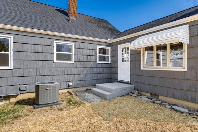 property entrance featuring crawl space, central air condition unit, a chimney, and a shingled roof