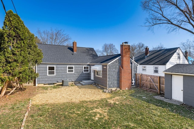 rear view of house featuring fence, central AC, roof with shingles, an outdoor structure, and a yard