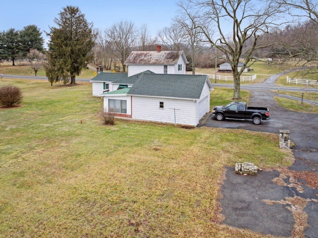 exterior space featuring aphalt driveway, a lawn, roof with shingles, and a chimney