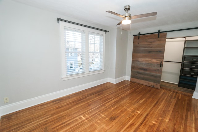 unfurnished bedroom featuring wood-type flooring, a barn door, and ceiling fan