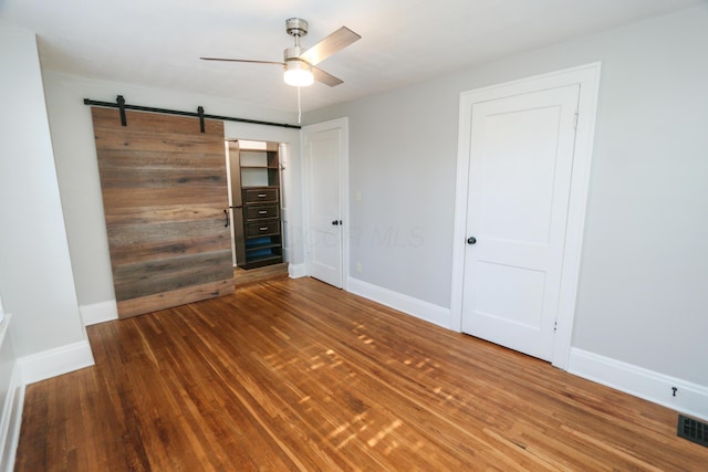 unfurnished room featuring hardwood / wood-style floors, a barn door, and ceiling fan