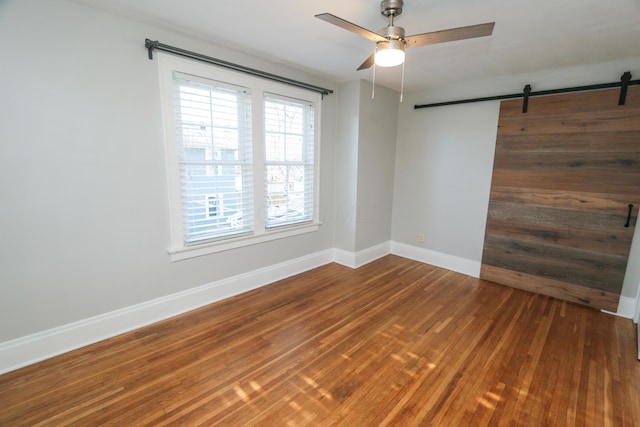 empty room featuring hardwood / wood-style flooring, a barn door, and ceiling fan