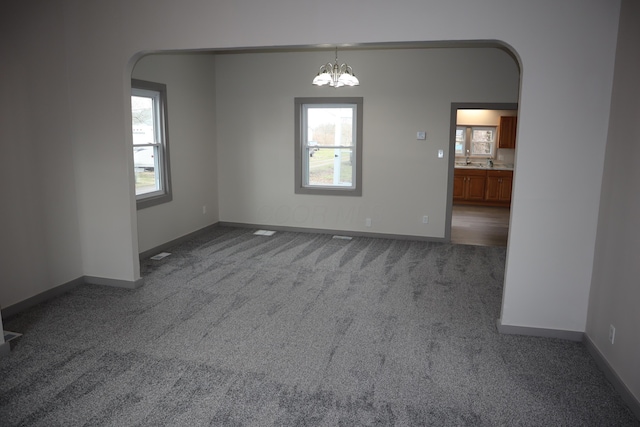 empty room featuring plenty of natural light, a chandelier, and carpet floors