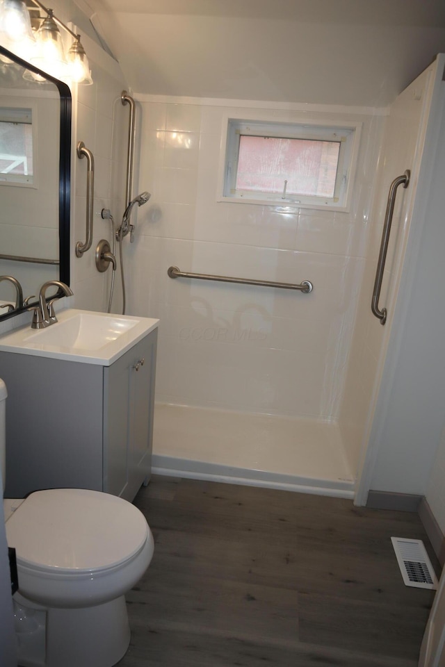 bathroom with wood-type flooring, tiled shower, vanity, and toilet