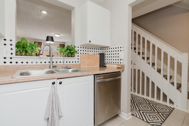 kitchen with tasteful backsplash, sink, white cabinets, stainless steel dishwasher, and light tile patterned floors