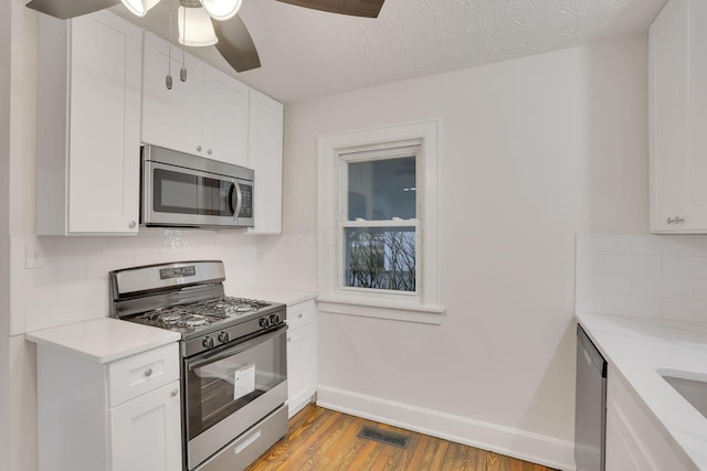 kitchen featuring light wood-type flooring, ceiling fan, stainless steel appliances, decorative backsplash, and white cabinets