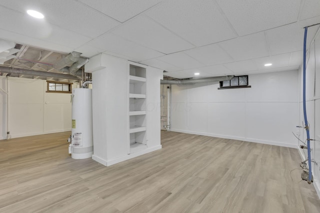 basement with built in shelves, light hardwood / wood-style flooring, and water heater