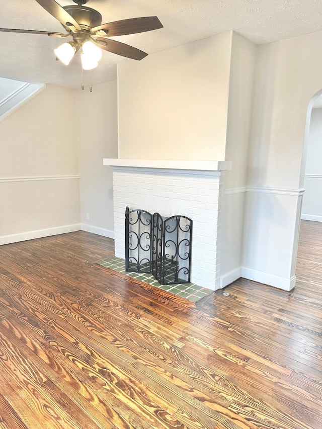 unfurnished living room featuring hardwood / wood-style flooring, ceiling fan, a brick fireplace, and a textured ceiling