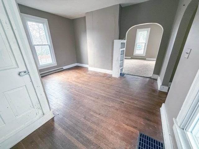 unfurnished room featuring a baseboard heating unit, dark wood-type flooring, and a wealth of natural light