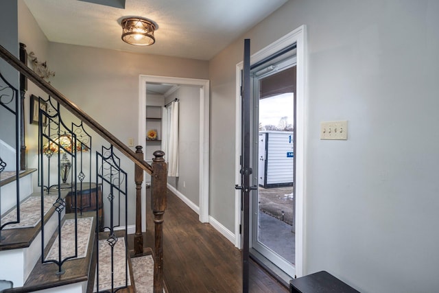 foyer with dark wood finished floors, baseboards, and stairs