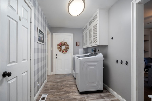 clothes washing area featuring wood finished floors, visible vents, baseboards, washer and dryer, and cabinet space