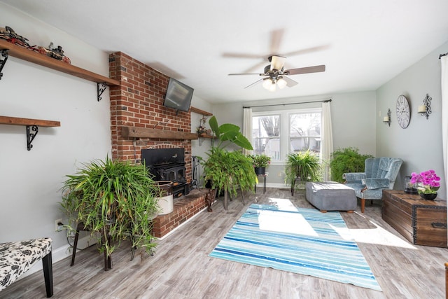 interior space with a wood stove, a ceiling fan, light wood-style flooring, and baseboards